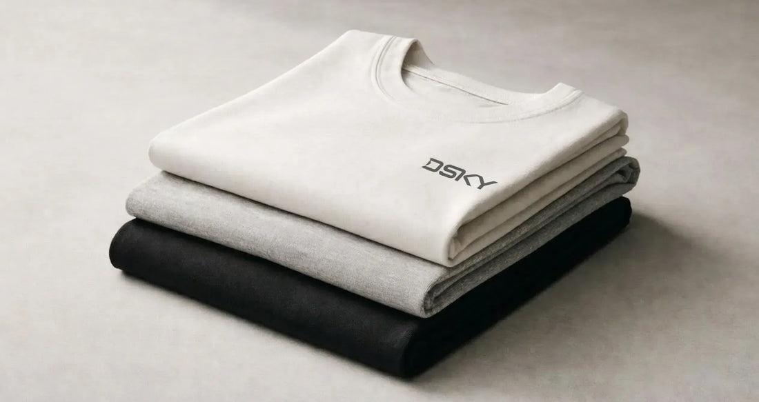 Gestapelde premium katoenen T-shirts in neutrale tinten met subtiel DSKY logo, minimalistische studiofotografie gericht op materiaal en stofstructuur.
