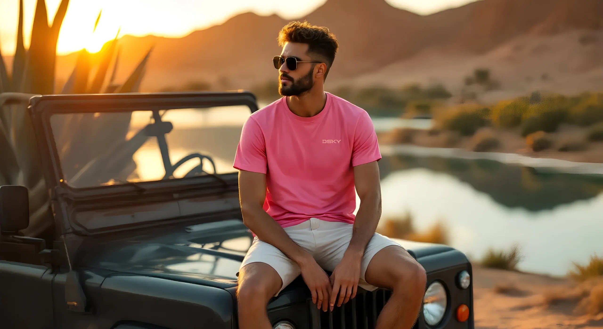 DSKY hero image capturing an authentic moment of reflection: a man wearing a premium dsky tee on a journey pauses, sitting on his vehicle by a calm lake to watch the sunset.