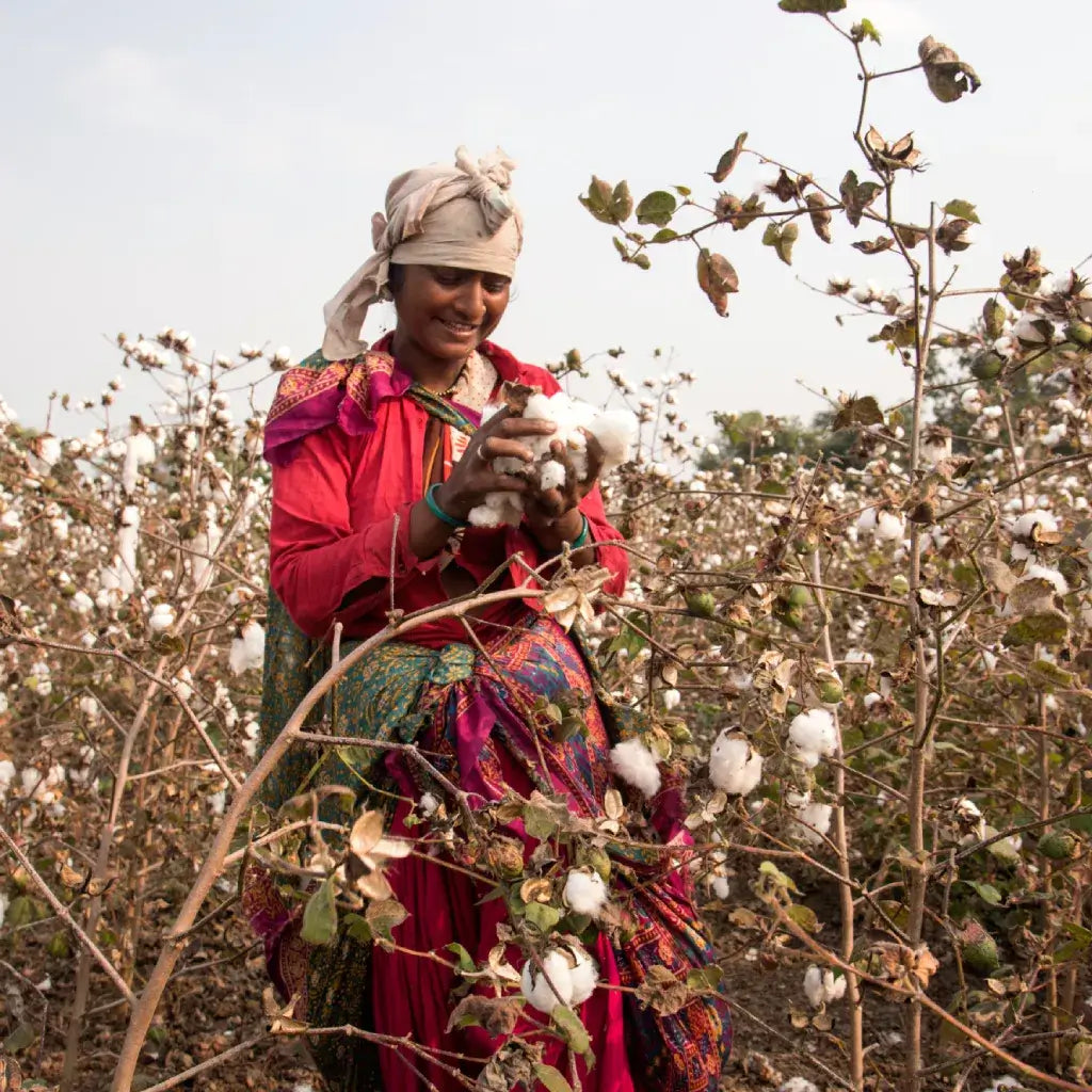 An authentic image representing DSKY's commitment to conscious choices: a farmer in a field, smiling as she holds freshly harvested organic cotton, connecting our premium materials back to their natural source.